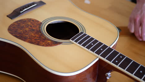 close up hands of a luthier craftsman adjusting and leveling the trussrod of an acoustic guitar neck fretboard on a wood workshop bench with lutherie tools slide right