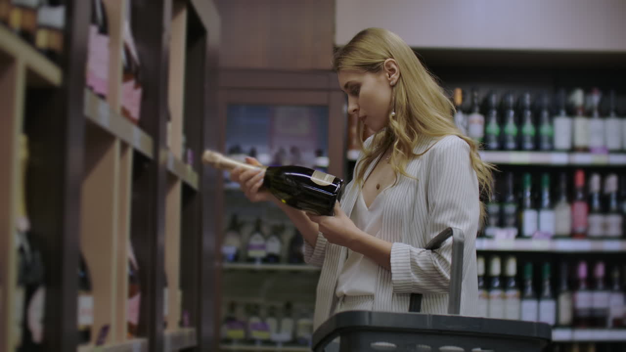 Woman chooses wine in the Supermarket customer selects product on the shelves in the store in. Alcohol sale. Read the label on the wine bottle.
