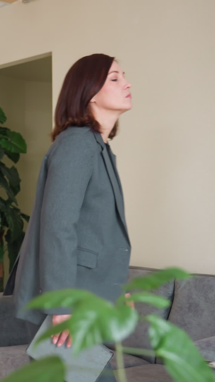 Professional businesswoman with brown hair walking through Eastern European office hallway while holding folder. Profile view captures confident stride in gray formal suit