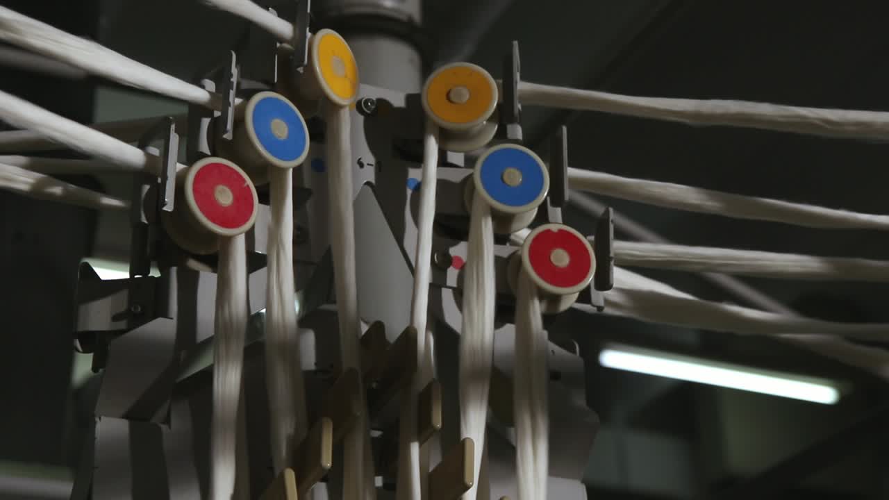 zoomado en una toma de una máquina de hilar, dentro de una fábrica de producción de lana, ya que sus múltiples ruedas van a una velocidad rápida con la lana