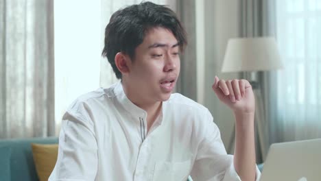 close up of asian man student raises hand and asks teacher a question while using computer to study online at home