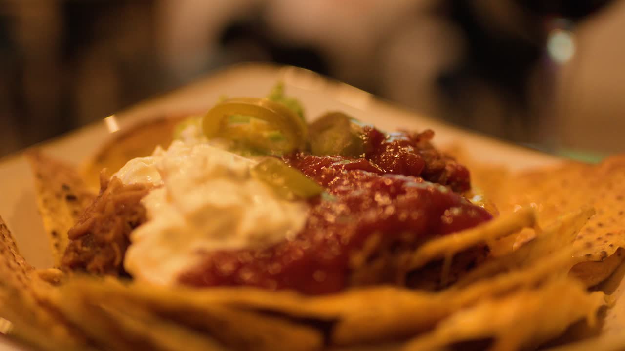 Mani che prendono nachos con salsa, panna acida, formaggio e jalapeños, con illuminazione calda e ambientale da ristorante