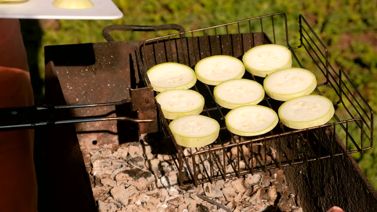 남자의 손은 석탄 그릴 위에 zucchini의 조각을 놓습니다.