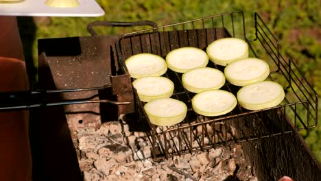 man's hand puts a slices of zucchini on top of charcoal grill.