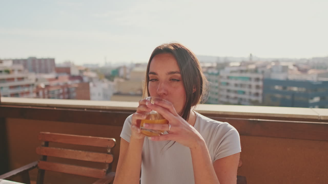 Woman drinking orange juice on balcony with city view