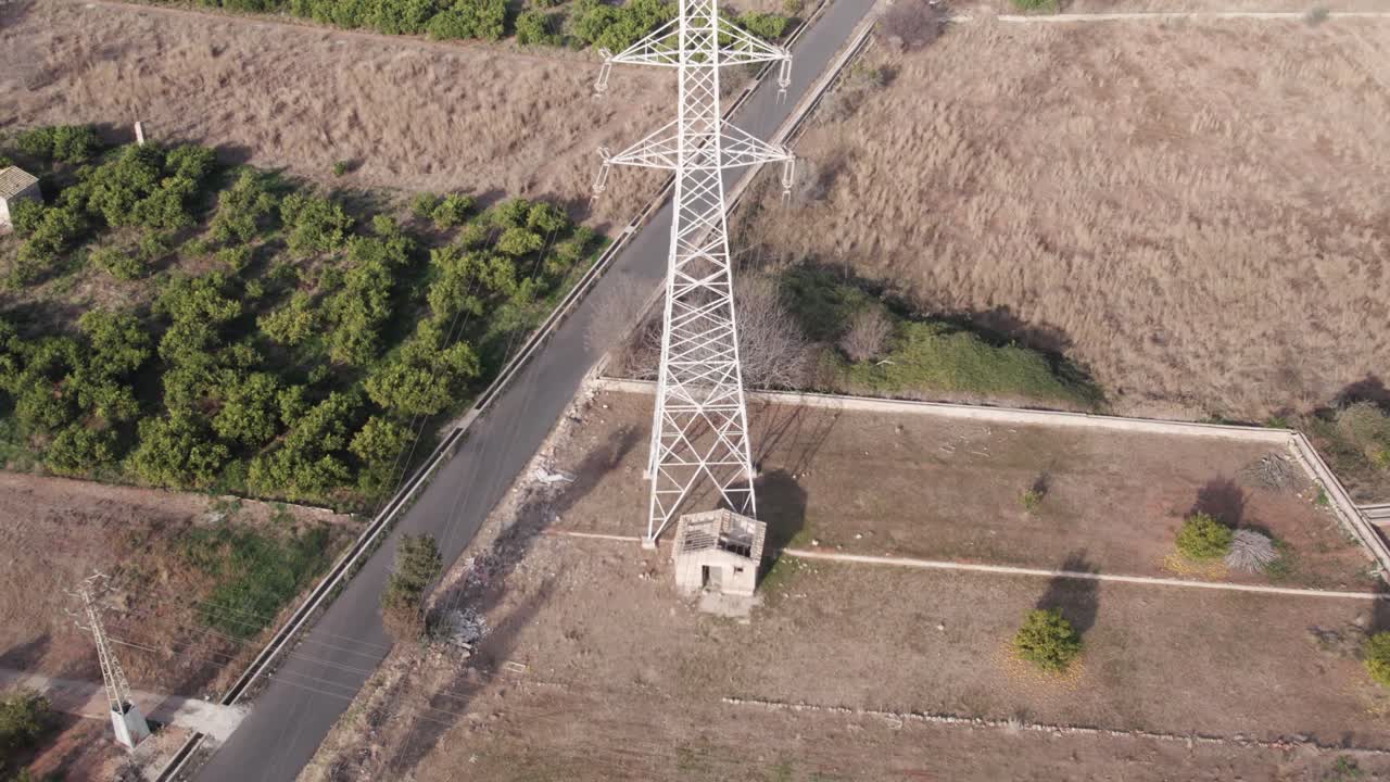 vuelo lento de drones sobre una torre de energía de alta tensión entre campos secos, mostrando los efectos de los campos electromagnéticos en la agricultura.