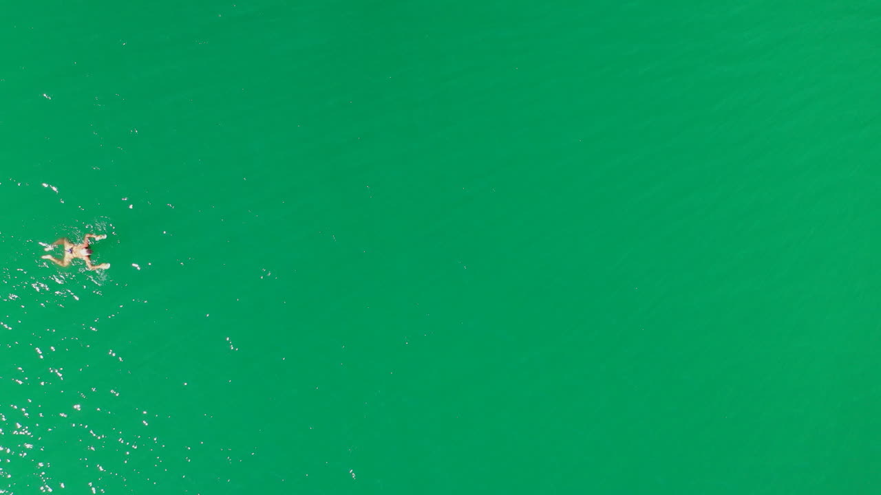 Aerial top down view of girl swimming breaststroke from left to right in green lake water, female fitness health and sports, shot from drone in 4k resolution