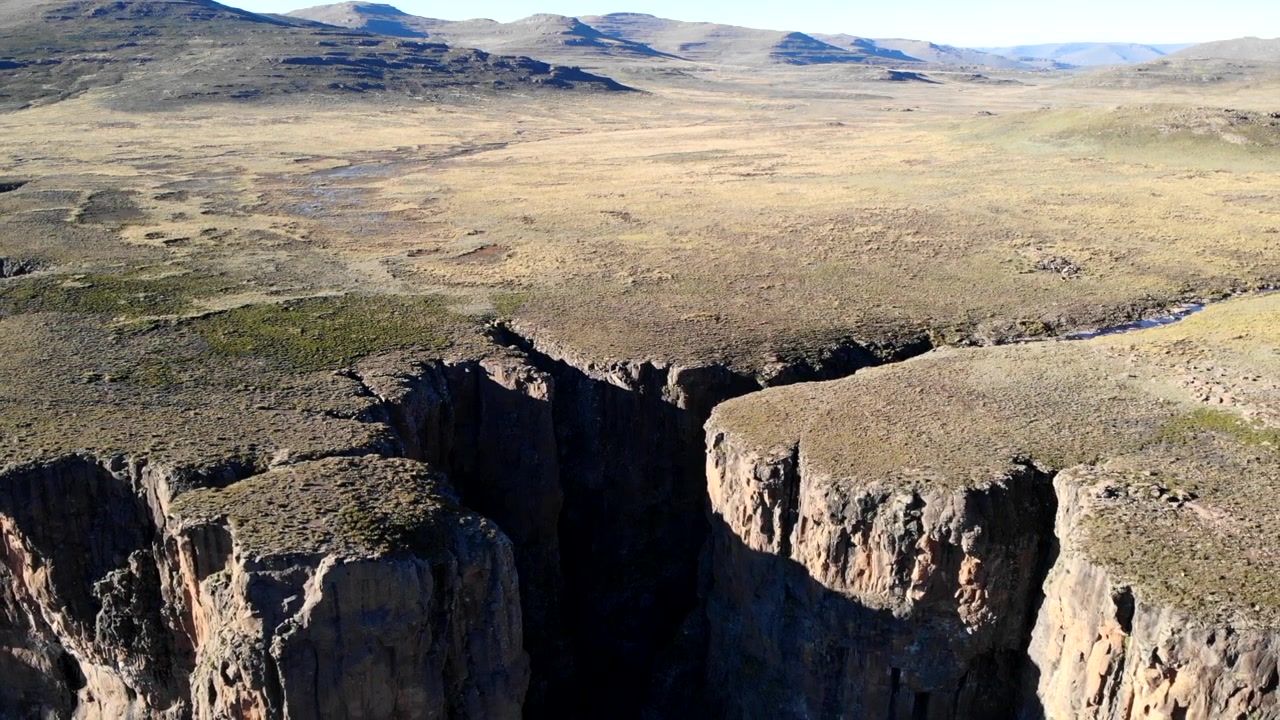 Ripresa aerea: profonda fessura di canyon in ombra, scogliere a picco che precipitano in una gola buia, fiume sottile che si snoda. Media