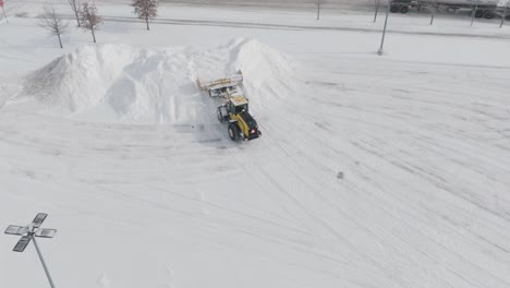 snow plow machine clearing snow into big piles for removal from parking lot. drone shot.