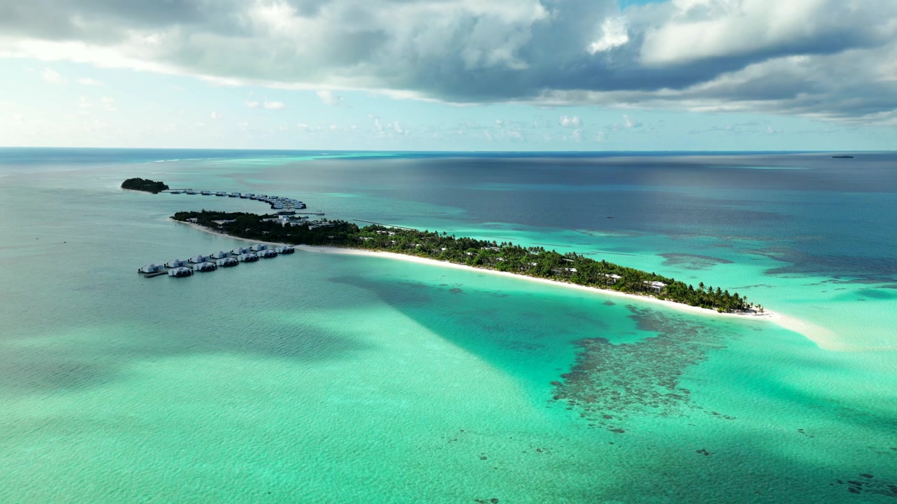 Isola resort delle Maldive con due moli di bungalow, spiaggia bianca, barriera corallina e ampio oceano turchese.