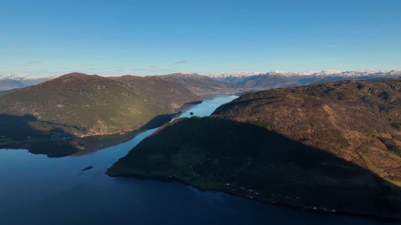 Panoramic aerial view over Etnefjord in Etne, Norway. Sunset colors over calm mirror-like water with distant snowcapped mountains in spring