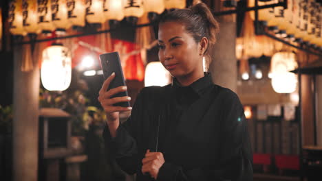 Young-woman-in-black-takes-a-selfie-within-a-Japanese-shrine-adorned-with-illuminated-lanterns