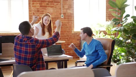 young team of three software developers finding problem solution while discussing code on laptop computer screen and celebrating it with high fives, tracking left shot