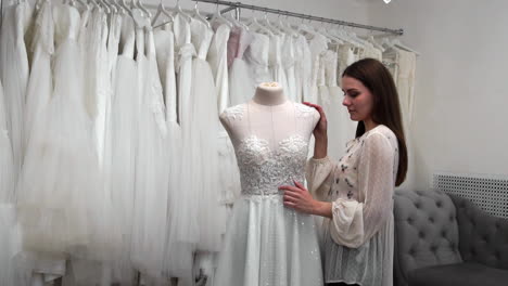 hermosa niña buscando vestido de novia en la cabina en comparación con otros vestidos. preparando para la boda. comprando un vestido de novia. la costurera inspecciona el vestido de novia hecho a medida terminado.