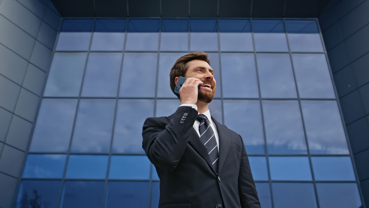 Businessman negotiating cellphone call outside office building smiling closeup