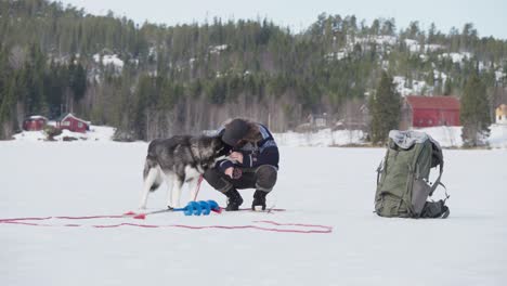 Rucksacktourist-Mit-Seinem-Hund-Beim-Angeln-Im-Zugefrorenen-See