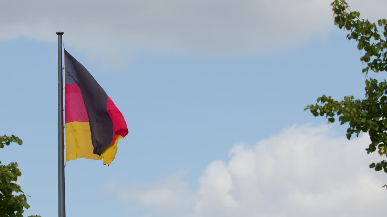La bandiera tricolore tedesca sventola su un palo argentato contro un cielo azzurro nuvoloso