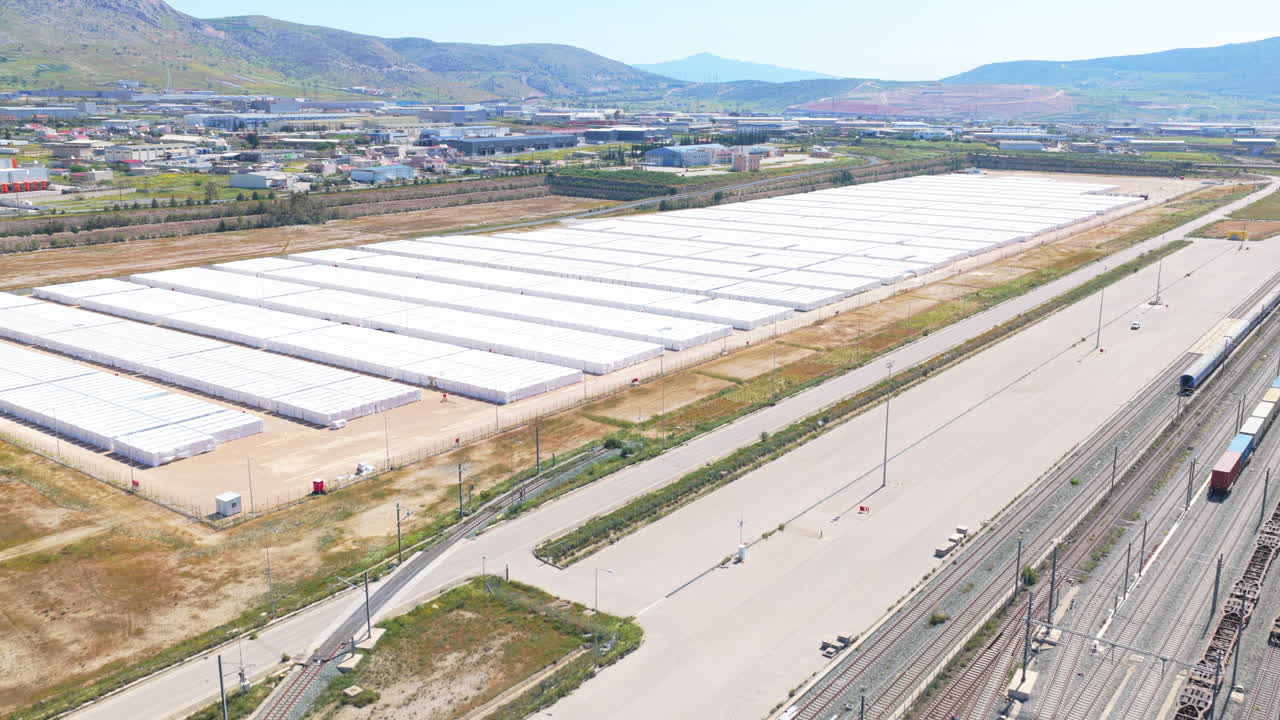 Riprese drone che catturano il complesso incrocio di sistemi di trasporto multimodale, con un cavalcavia autostradale che attraversa un vasto terminal merci ferroviario e un centro di distribuzione logistica