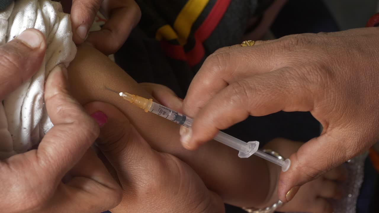 Social healthcare ASHA worker giving polio vaccine injection on arms of infant child to prevent poliovirus infections in rural Indian town, Begusarai, Bihar