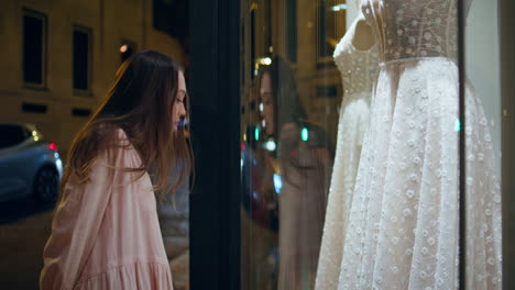 girl looking wedding store showcase standing on night street closeup. white gown