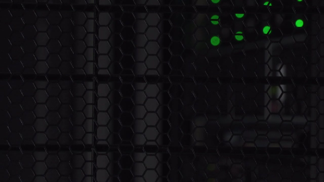 Grønne prikker skinner bag et dataskab i stål med bikube-design i et mørkt computerrum