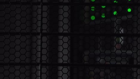 Green-dots-shining-behind-a-honeycomb-design-steel-data-rack-in-a-dark-computer-room