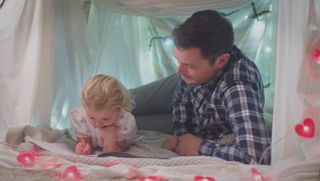 Padre-E-Hija-Pequeña-Con-Libro-Para-Colorear-En-Un-Campamento-Casero-En-El-Dormitorio-De-Un-Niño-En-Casa---Filmados-En-Cámara-Lenta