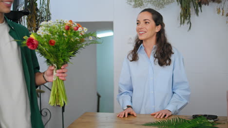 mujer de venta sonriente da flores ramo a hombre africano positivo comprador en la tienda