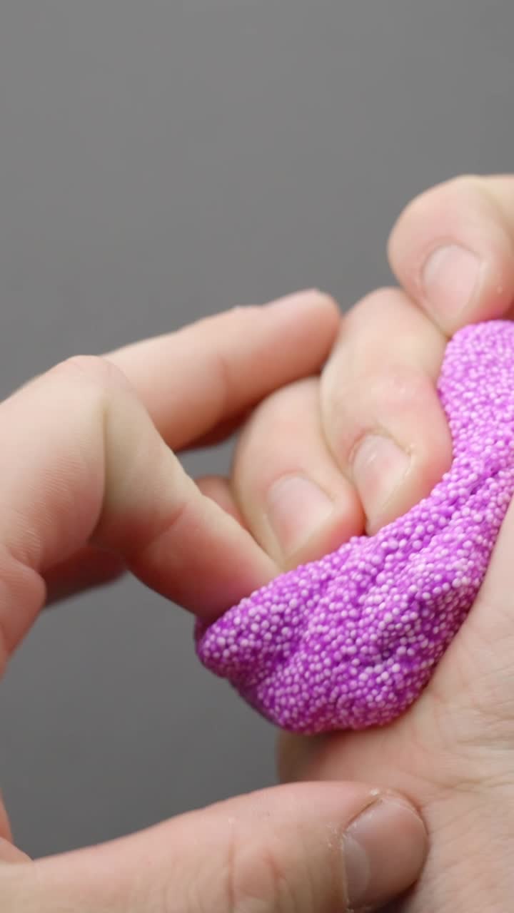 Hand pressing vibrant purple bead slime in sensory play close-up, vertical