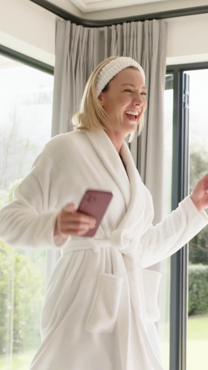 Vertical video: Tapping red phone, woman in white robe dancing by glass doors, controlling music