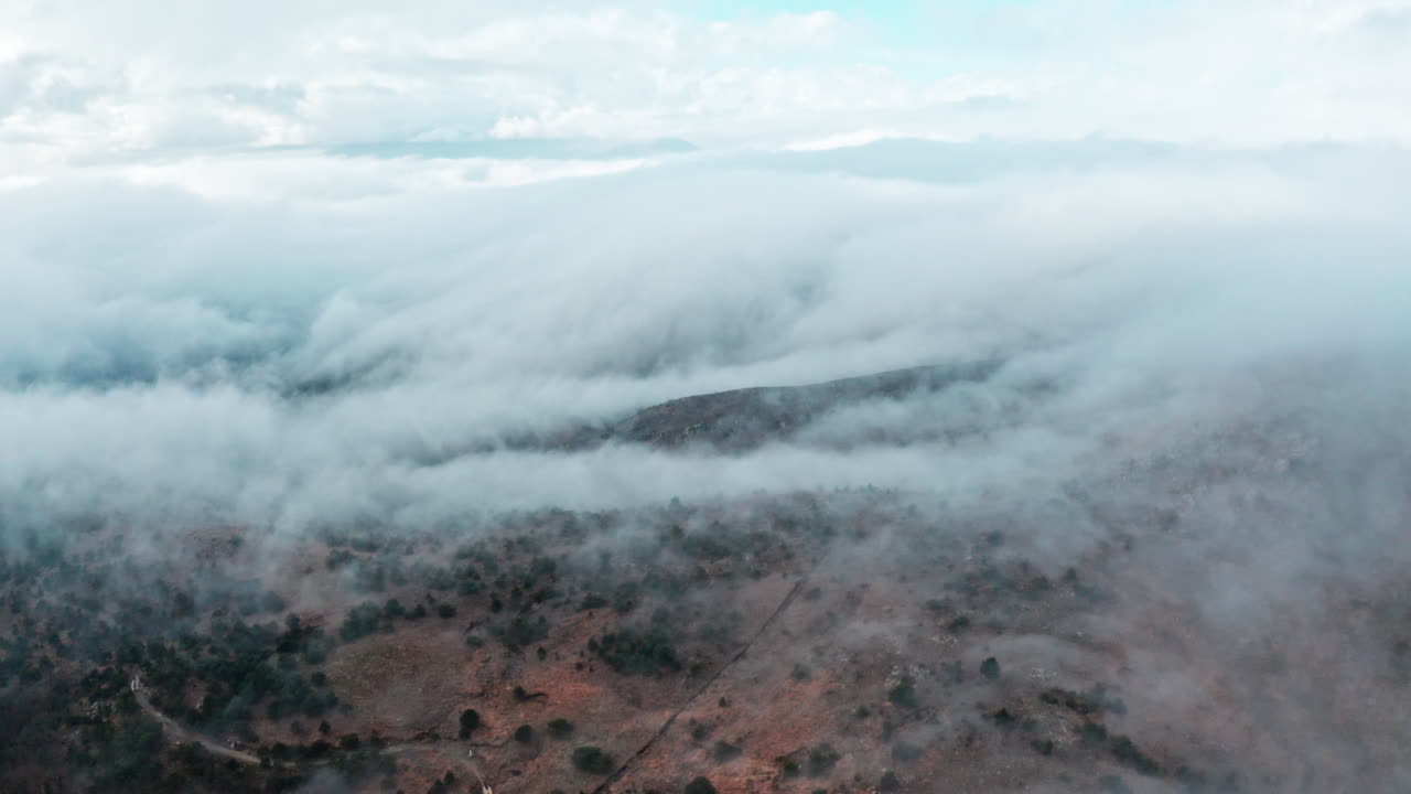 nubes de niebla rodando sobre un paisaje de montaña seco al amanecer, vista aérea