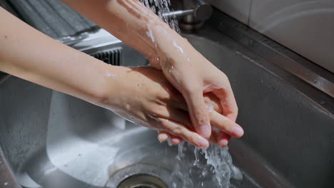 hands of woman wash their hands in a sink with soap foam to wash the skin and water flows through the hands