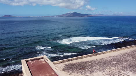 vast, blue ocean of los lobos island and a woman strolls by a monument