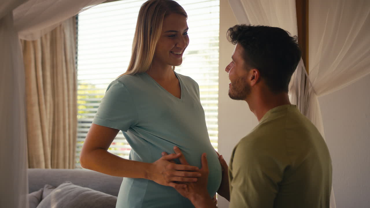 Couple With Pregnant Woman In Bedroom At Home With Man Feeling Baby Kicking