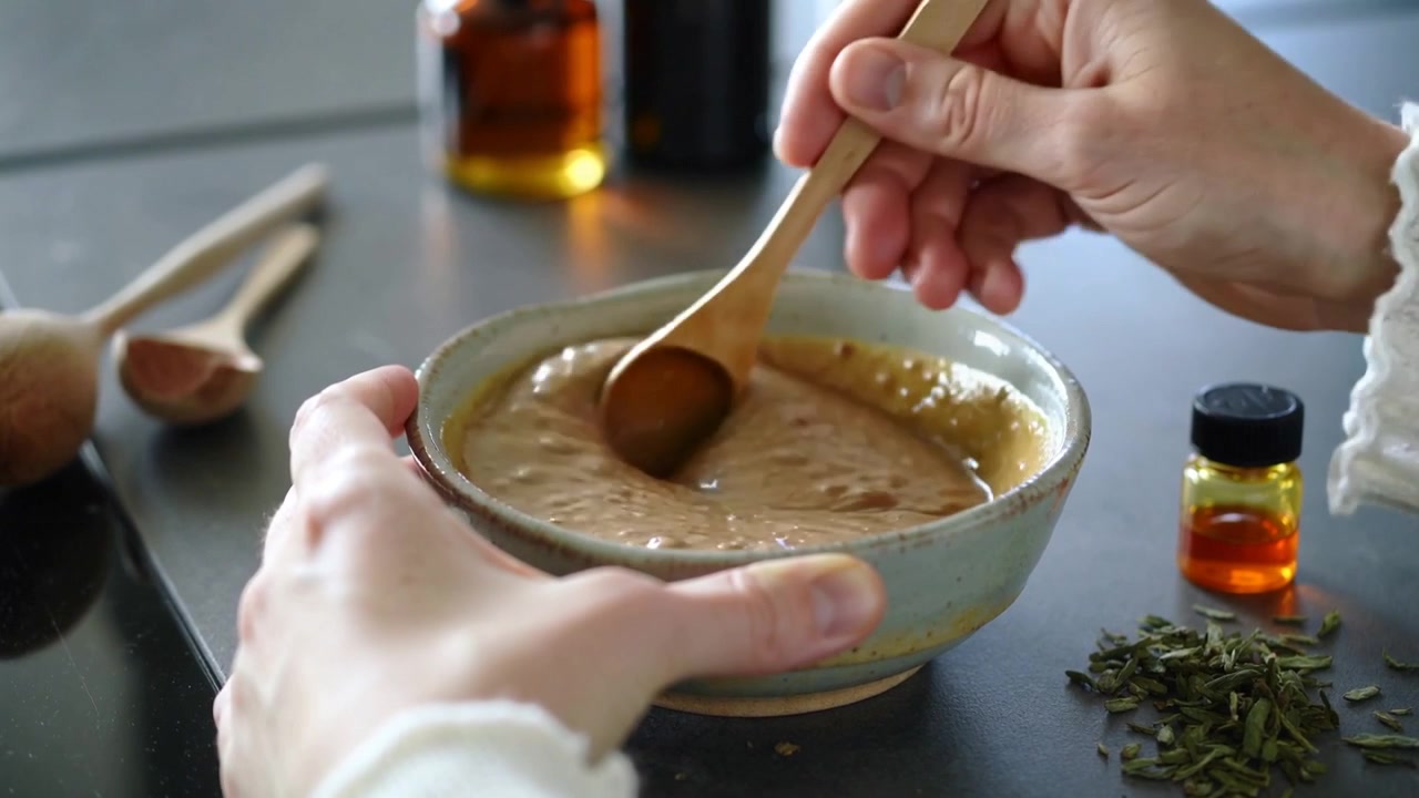 Lifting right hand, mixing paste to smooth in bowl on kitchen counter with spoon knit sleeve