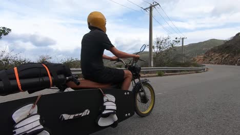 man rides motorbike transporting surfboard and kitesurfing equipment