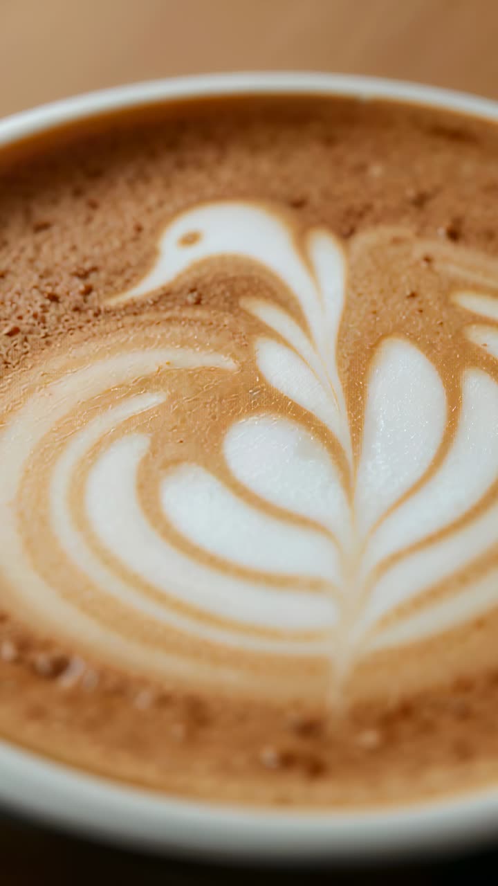 Vertical video: Zooming camera focusing on white cup, showing swan foam texture on wood table