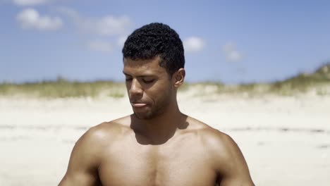 calm black man meditating on a beach, smiling with peace and tranquility, and with praying hands