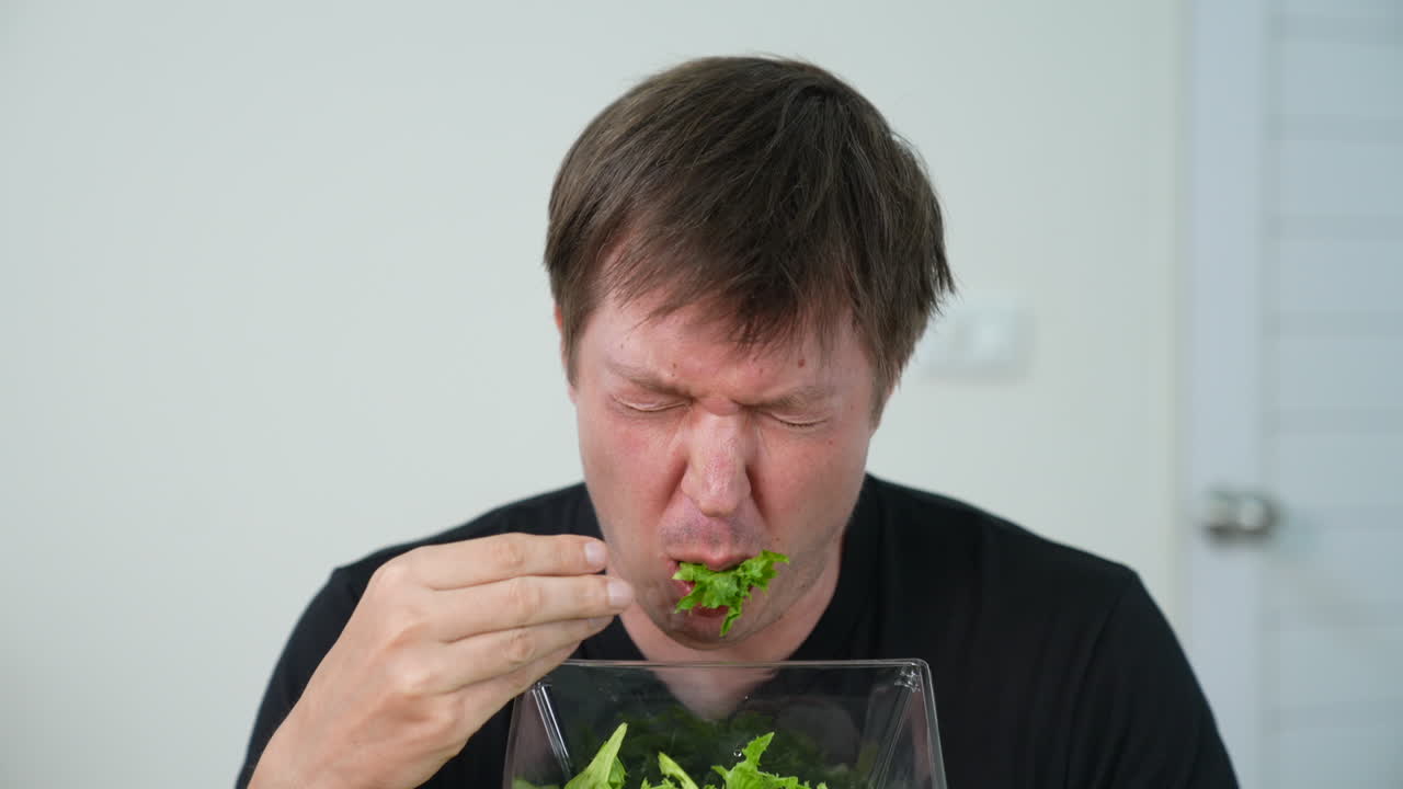 Disgusted man sitting alone and trying to eat salad but spitting it out showing dislike