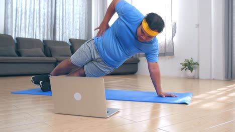 fat man doing exercises at home while looking at his laptop