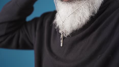 religious christian man with white beard hangs cross necklace around his neck.