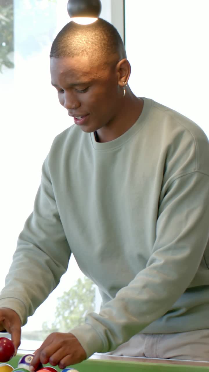 Vertical video: Approaching man in green sweater racking pool balls on table preparing shot