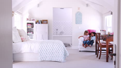 happy young female friends sitting in armchair in a bedroom