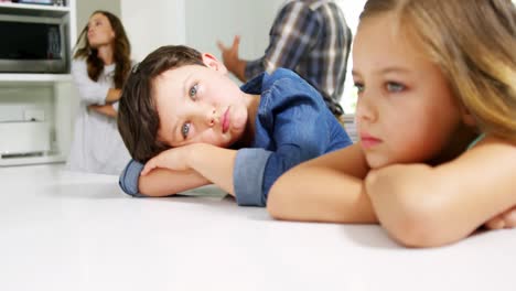 hermanos de aspecto triste con sus padres peleando detrás de ellos