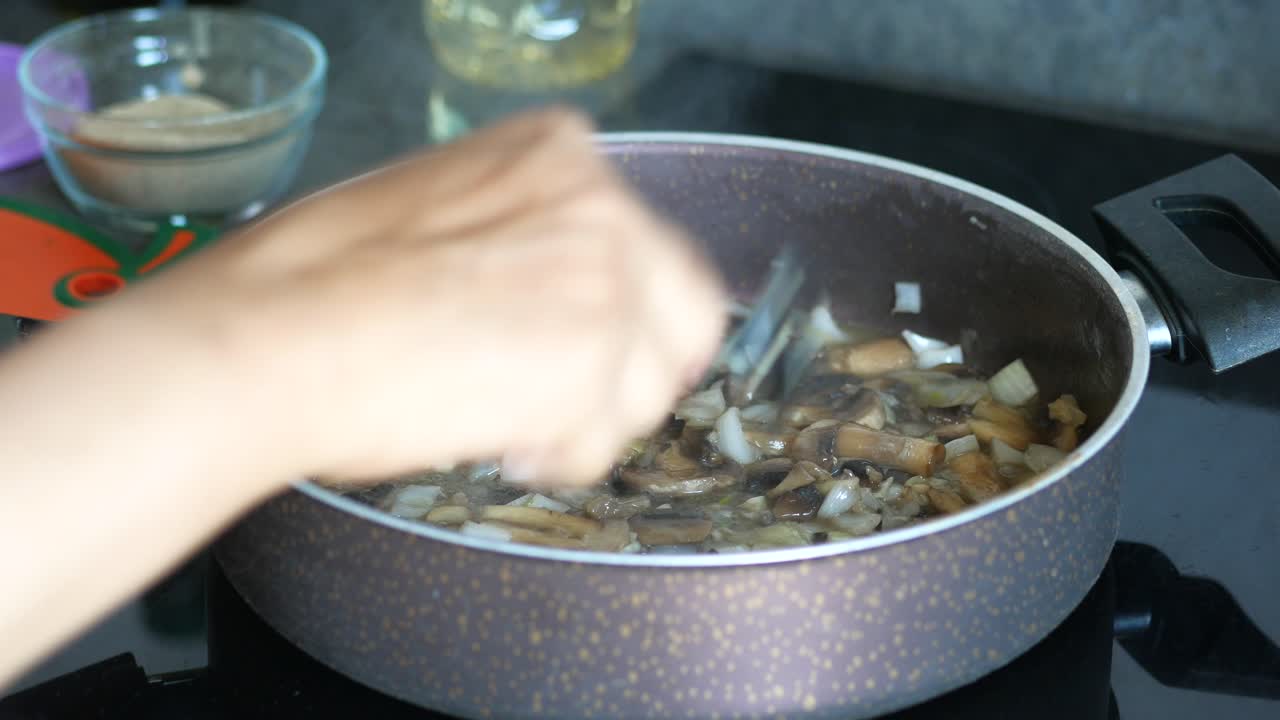 Close-up of a person cooking mushrooms and onions in a pan
