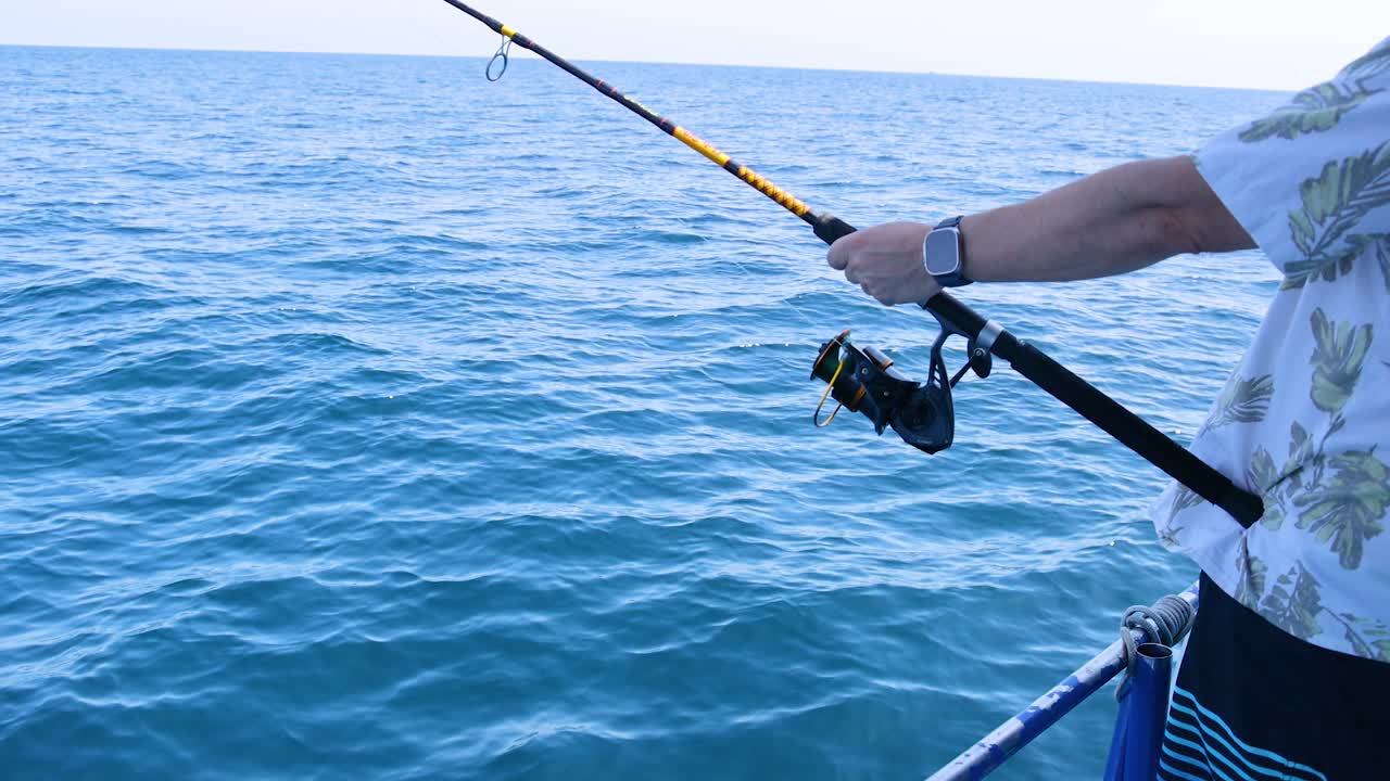 una persona pescando desde un barco en phuket, tailandia, bajo cielos despejados con mar tranquilo y luz del día brillante