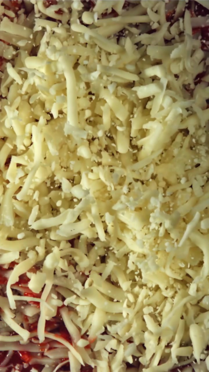Primo piano di mozzarella grattugiata cosparsa su salsa rossa