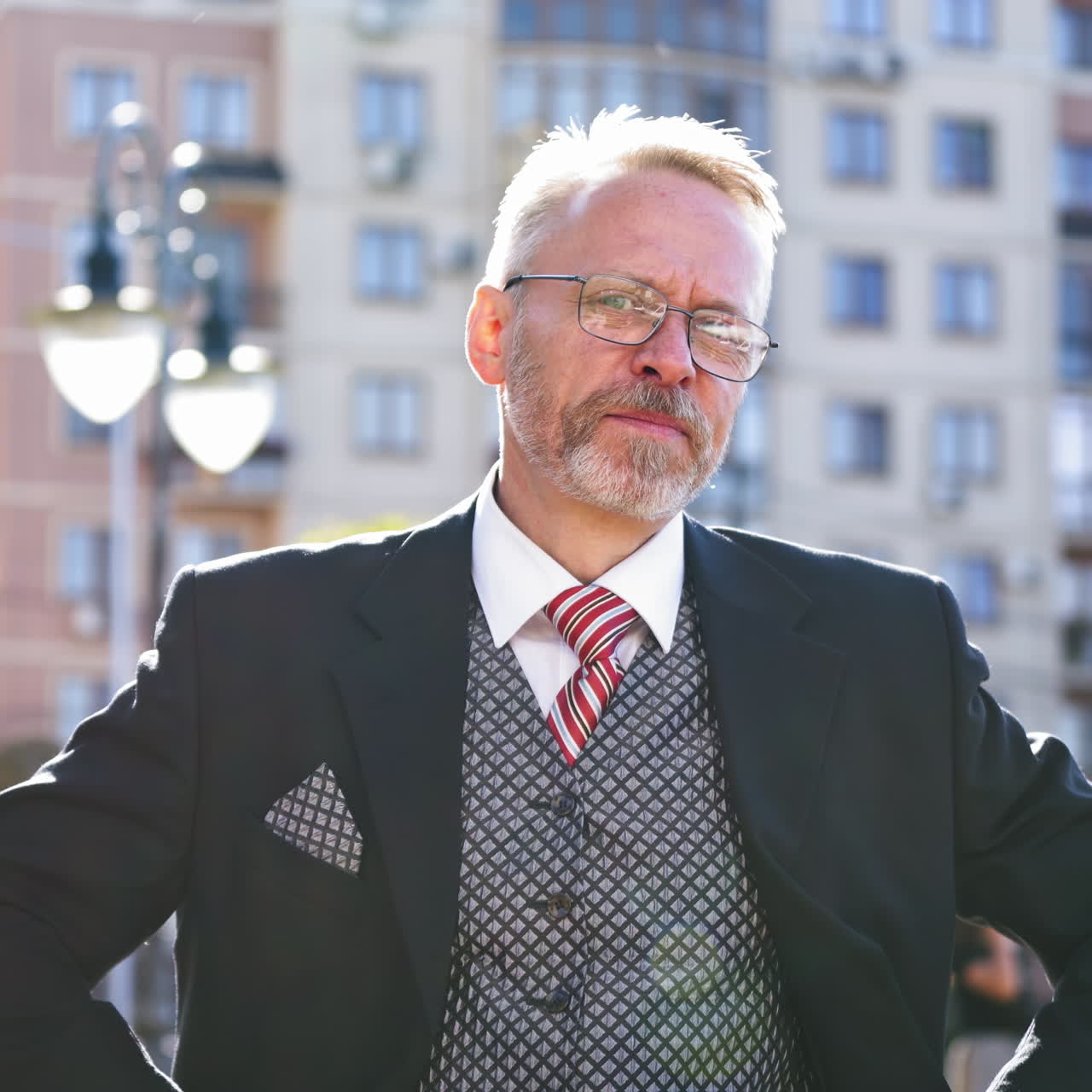 Senior businessman in glasses and suit talks happily on the city background. Enthusiastic middle aged man talking and showing happy gesture with his arms.