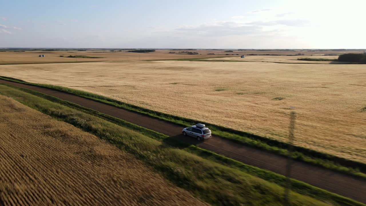 대초원에서 일몰 동안 먼지가 많은 시골길을 따라 운전하는 은색 자동차의 공중 4k 샷