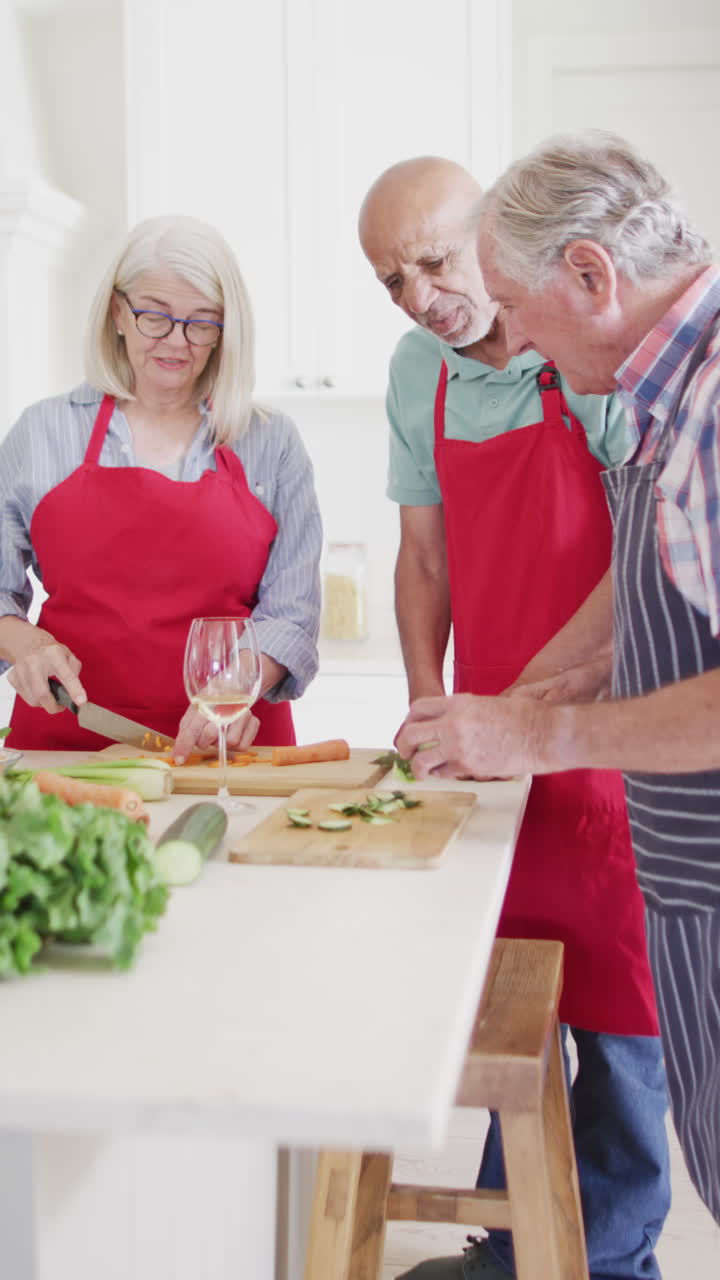Vertical video of diverse senior male and female friends preparing food in kitchen, slow motion